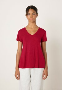 Raudona v-vieno marškinių su trumpomis rankovėmis, pagaminti iš lengvo audinio; turi laisvą siluetą ir šiek tiek tekstūruotą paviršių.