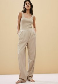 Top de tirantes acanalado beige con escote cuadrado, combinado con pantalones beige de pierna ancha y cintura alta, que cuentan con pliegues frontales y bolsillos laterales.