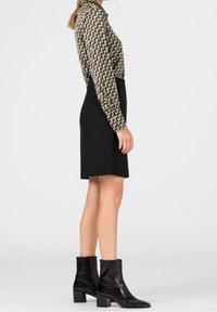 Black dress with a geometric patterned long-sleeve blouse; paired with black leather ankle boots featuring a block heel.