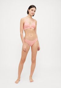 Rózsaszín mintás bikini szett, amely egy triangle bralette-ből áll vékony pántokkal, és hozzá illő, alacsony derekú alsóból. A ruha rugalmas anyagból készült.