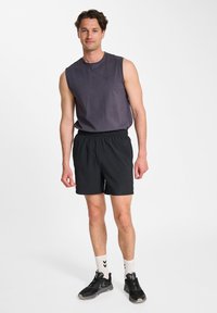 Ärmlös grå skjorta med rund halsringning, i kombination med svarta shorts. Svarta sneakers och vita strumpor med svarta ränder kompletterar looken.