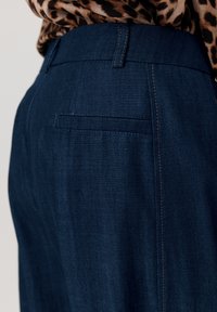 Ciemnoniebieskie dżinsy o dopasowanym kroju, czystych liniach, subtelnym haftowaniu i tylniej kieszeni. Materiał ma gładką teksturę.