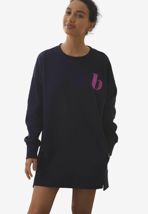 Marine sweatshirt jurk met lange mouwen, zijsplitsingen en een roze geborduurde letter 'b' op de borst, gemaakt van een zachte stof.