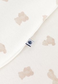 Bawełniana poszewka na poduszkę z delikatnym białym tłem i jasnobeżowymi wzorami niedźwiedzi. Na krawędzi znajduje się mała granatowa metka.