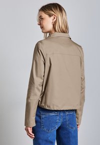 Beige kort jacka med en slät textur och klassisk krage. Har lång ärm och en minimalistisk design. Bärs med blå denimjeans.