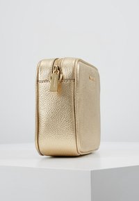 Bolso de cuero texturizado dorado con cierre de cremallera y base plana. Presenta un logo discreto y bordes redondeados para un diseño rectangular compacto.