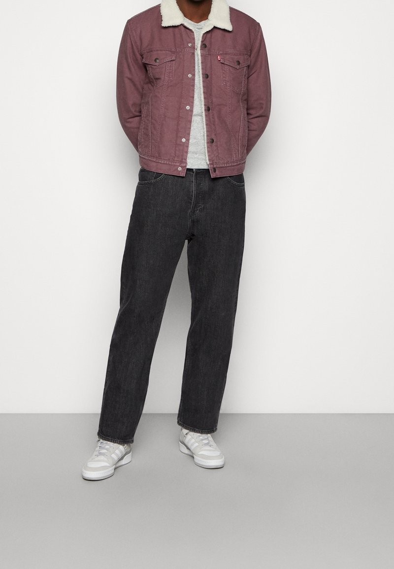 Rosa denimjacka med en vit fuskpälskrage, grå skjorta under, svarta raka jeans och vita sneakers. En enkel, avslappnad outfit.