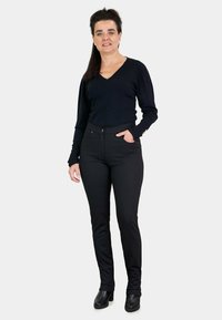 Suéter negro de cuello en V combinado con pantalones ajustados negros con estampado y botas negras de tobillo. Colores sólidos con detalles de textura sutiles visibles.