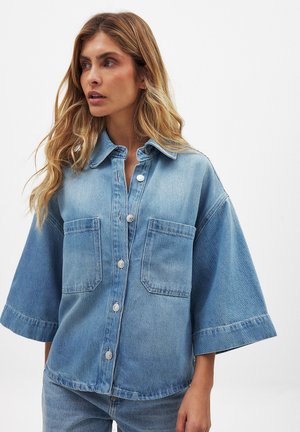 Giubbotto di jeans in blu chiaro, con colletto a risvolto, chiusura frontale con bottoni, due tasche sul petto e maniche ampie. Vestibilità leggermente oversize.