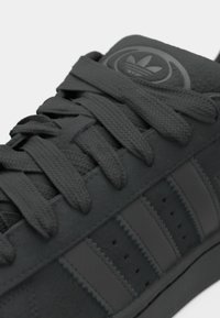 Svarta träningsskor med en texturerad mockaöverdel, platta snören, tre ränder design och en rund logotyp på tungan. Slät gummisula.