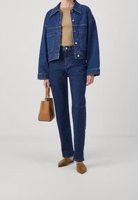 Tumma sininen farkkutakki, jossa on taskut ja napit, yhdistetty tummansinisiin korkeavyötäröisiin farkkuihin. Mukana ruskea laukku ja teräväkärkiset kengät.