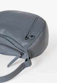 Grijze leren tas met een gladde textuur, ronde vorm, ritssluiting en een platte schouderriem. Kenmerkt zich door minimalistische ontwerpaccenten.