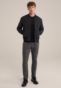 Černá bomber bunda, svetr s kulatým výstřihem, šedé kostkované kalhoty a černé šněrovací boty. Hladká látka s přiléhavým střihem.