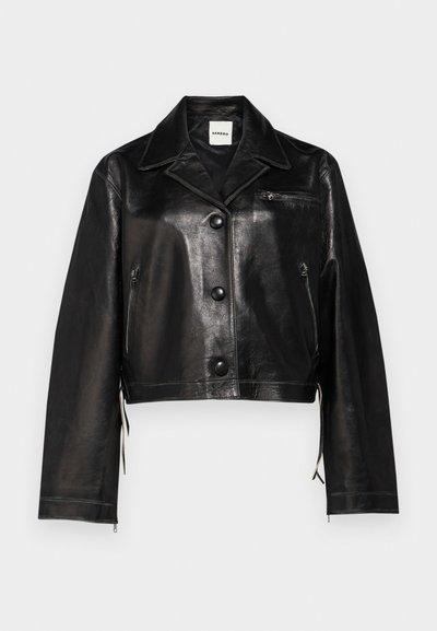 Μαύρο δερματίνι κοντό μπουφάν με καμπύλο γιακά, μπροστινά κουμπιά, πλαϊνές φερμουάρ και λεπτομέρεια τσέπης στο στήθος. Λείο υφάσμα και εφαρμοστή σχεδίαση.