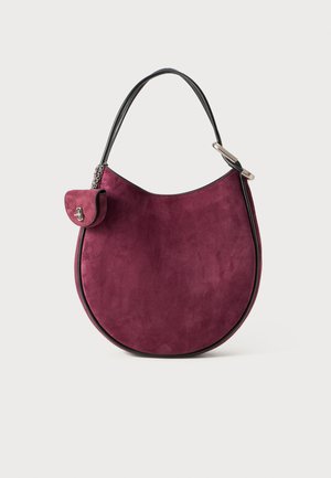 Bolso de ante púrpura con forma redondeada, ribetes en negro y asa corta. Cuenta con un pequeño bolsillo con solapa y detalles en plata.
