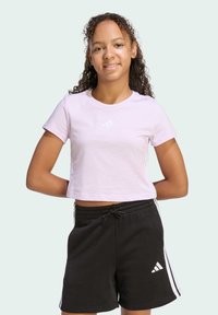 Svijetlo ružičasta kratka majica s malim bijelim adidas logom i crne kratke hlače s dvije bijele pruge i adidas logom na lijevoj nozi.