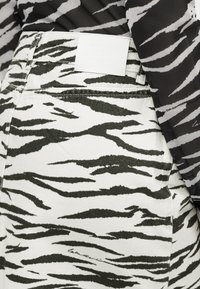 Λευκή τζιν φούστα με μοτίβο μαύρες ρίγες τίγρης, με ετικέτα επωνυμίας στη μέση, υφασμάτινη υφή και διακριτικές ραφές.