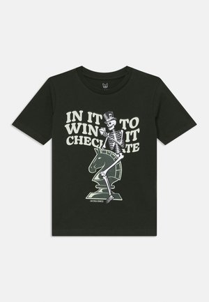 T-shirt di cotone verde scuro con grafica di uno scheletro in cilindro che tiene delle carte, con il testo "IN IT TO WIN IT." La taglia non è specificata.