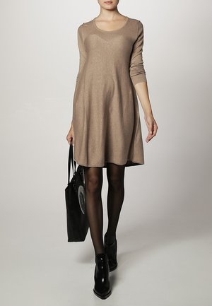 Beige long-sleeve dress with a scoop neckline, flowing A-line silhouette, and soft texture; paired with a black shoulder bag and black heels.