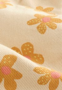 Blumenmusterstoff mit beigem Hintergrund; zeigt orangefarbene Blumen mit pinken Mittelpunkten und gelben Akzenten; strukturierter Webeindruck sichtbar.