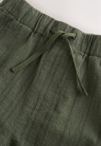 Close-up of green drawstring elastic waistband on textured fabric pants.