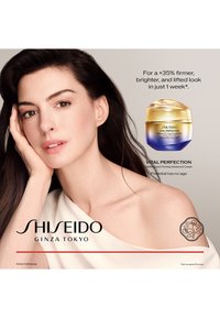 Crème Shiseido Vital Perfection dans un pot rond avec un couvercle dégradé or et bleu, offrant des effets raffermissants et éclaircissants.