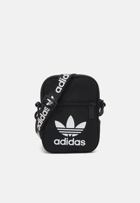 Černá crossbody taška z odolného materiálu s výrazným bílým logem Adidas a nastavitelným popruhem s detaily loga.