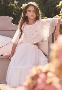 Top blanco con bordado floral y mangas transparentes, acompañado de una falda larga de tul blanca. Ajuste cómodo, textura en capas y tela suave.