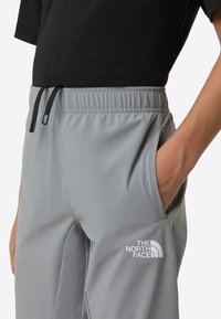 Lys grå treningsbukser med elastisk midjebånd, svarte snorer, sidelomme og en hvit logo på lårområdet.