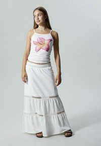 Hvid maxi-nederdel med blonderkanter og flæser, parret med en tætsiddende hvid tanktop med et stort pink blomsterprint.