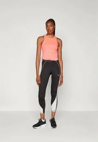 Ružová športová tielko s pretekárskym strihom, v kombinácii s čiernymi legínami so bielymi bočnými akcentmi a logami. Čierne športové topánky.