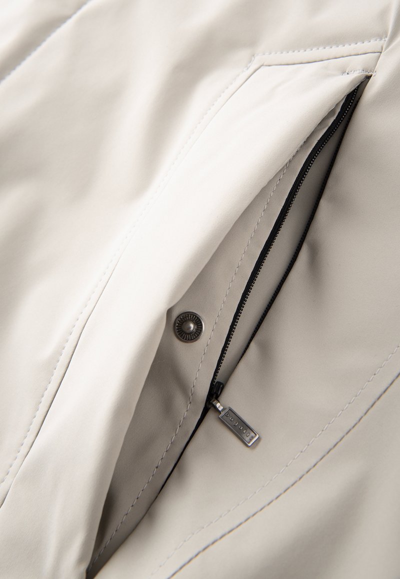 Tissu de veste beige clair avec une texture lisse, doté d'une fermeture éclair noire, de matériel en argent et d'une poche latérale pour le stockage.