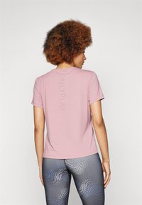 Pink athletic t-shirt with a round neckline and short sleeves. Features "ONLY PLAY" printed vertically in a shiny accent. Worn with patterned gray leggings.