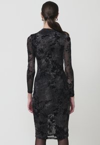 Rochie florală neagră cu mâneci lungi transparente, siluetă ajustată, țesătură texturată și margine de lungime medie. Are o deschidere în spate.