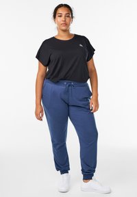 Black short-sleeve t-shirt with a subtle logo, paired with navy blue joggers featuring a drawstring waist and ribbed cuffs, worn with white sneakers.