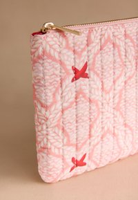 Rosa quiltad necessär med flätat mönster, röda fågeldesigner och dragkedjebeslag i guld mot en beige bakgrund.