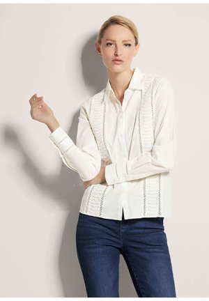 Witte overhemd met ruches en geborduurde accenten aan de zijkanten, gecombineerd met donkerblauwe slim fit spijkerbroek.