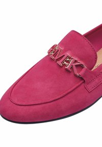Fuchsia suède loafer met een platte zool, voorzien van een metalen kettingaccent en reliëfletters over de voorkant. Glad textuur.
