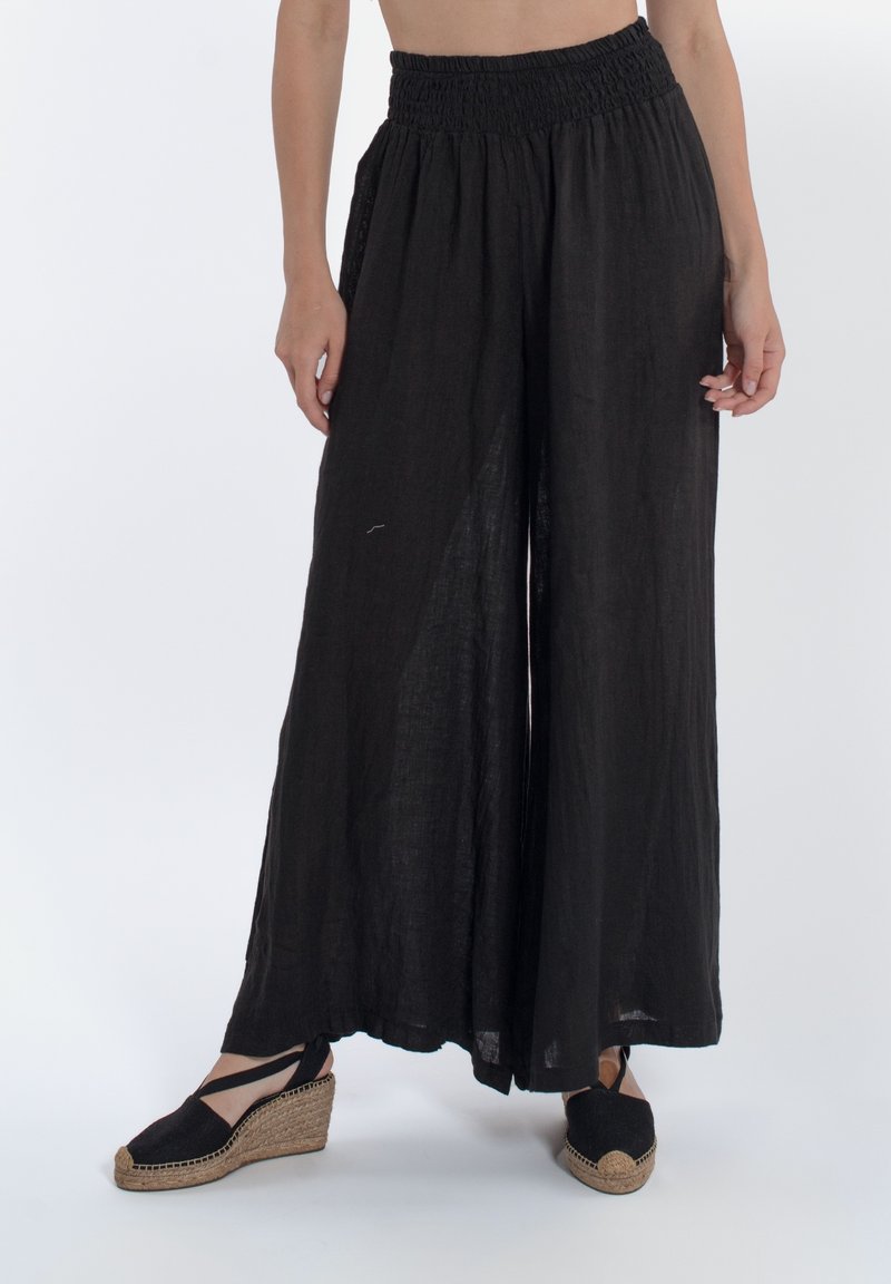 Pantaloni neri a gamba larga in lino leggero con vita arricciata. Indossati con zeppe espadrillas nere per una vista a lunghezza intera.