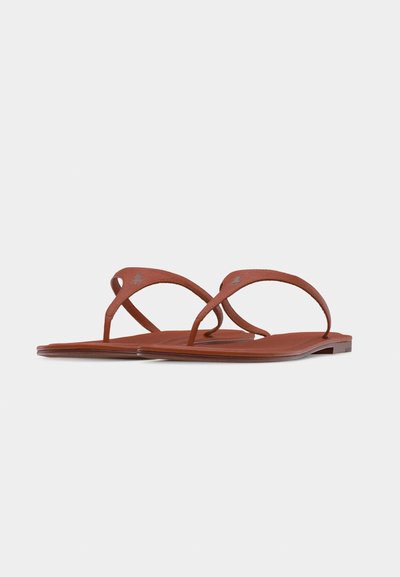 Ζευγάρι καφέ επίπεδων σανδαλιών με λεπτούς διασταυρωμένους λουριά και μινιμαλιστικό σχέδιο σε απλό ανοιχτό φόντο.