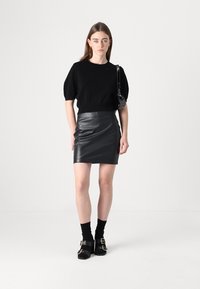 Svart, kort puffermet genser kombinert med et tettsittende svart skinnskjørt. Tilbehør med en liten svart veske og svarte sokker med sandaler.