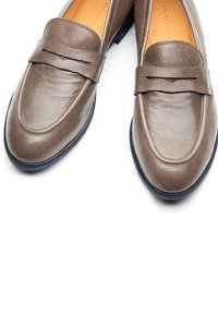 Braune Leder-Loafer mit glatter Textur, verziert mit einem dekorativen Riemen und dezenten Nahtdetails. Schwarze Gummisohle für Griffigkeit und Haltbarkeit.