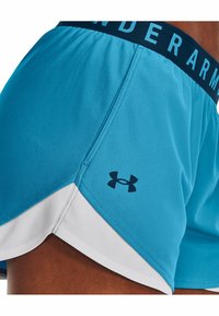 Pantalones deportivos azules con un dobladillo blanco, que cuentan con una cintura elástica azul oscuro con el texto "Under Armor" y un pequeño logo negro en el lateral.