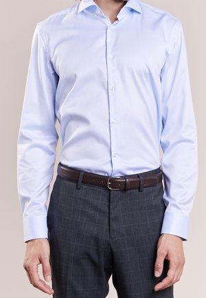 Chemise à manches longues bleu clair avec un col boutonné, tissu lisse, associée à un pantalon à carreaux gris foncé et une ceinture en cuir marron.
