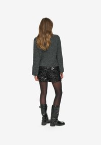 Grå striktrøje, sorte palietshorts, sorte strømpebukser og sorte støvler til knæet. Har en afslappet pasform med struktureret materiale og skinnende detaljer.
