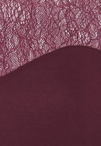 Tissu bordeaux profond avec une couture diagonale séparant un tricot lisse en dessous d'un motif de dentelle complexe au-dessus.