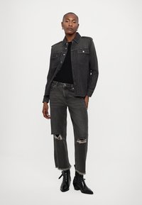 Hallhalli denimjakk, millel on kaks rinnataskut, koos kulunud hallide teksadega, millel on narmendavad ääred. Mustad ankle-boots lõpetavad välimuse.