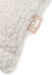 Tissu flou de couleur blanc cassé avec un motif texturé, agrémenté d'une petite étiquette beige sur le bord portant un logo "J".
