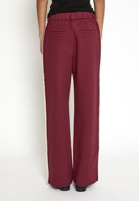 Burgundy wide-leg pants with an elastic waistband, featuring two back pockets and contrasting cream side stripes. Smooth fabric texture.