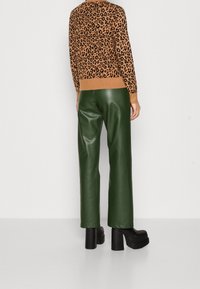 Úpletový svetr s leopardím vzorem v hnědé a černé barvě, kombinovaný s vysokým pasem zelených kožených kalhot a robustními černými platformovými podpatky.